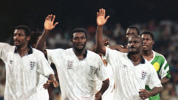 Les joueurs de l'équipe du Cameroun (de gauche à droite,&nbsp;Omam Biyick, Stephen Tataw et Roger Milla) saluent le public après leur élimination cruelle en quart de finale de la Coupe du monde 1990 contre l'Angleterre, dont certains joueurs portent le maillot après la rencontre. (GEORGES GOBET / AFP)