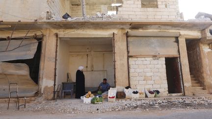 Un vendeur de&nbsp;fruits&nbsp;devant des bâtiments détruits à Qmenas, dans le nord-ouest de la Syrie, le 30 juin 2015. (AMMAR ABDULLAH / REUTERS)