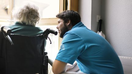 Un homme apporte son soutien à une personne agée en fauteuil roulant. Photo d'illustration. (CHRISTIAN BEUTLER / MAXPPP)