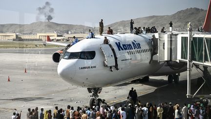 Des Afghans grimpent sur un avion, à l'aéroport de Kaboul (Afghanistan), le 16 août 2021. (WAKIL KOHSAR / AFP)