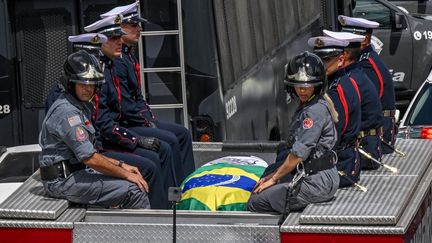 Des pompiers accompagnent le cercueil du "Roi", recouvert des drapeaux du Brésil et du club de Santos, à la sortie du stade, avant un cortège funèbre dans les rues de la ville. (NELSON ALMEIDA / AFP)