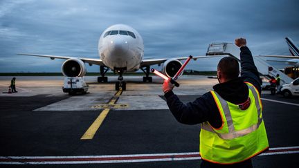 Un employé de l'aéroport de Roissy Charles de Gaulle guide l'arrivée d'un avion de ligne. Photo d'illustration. (MARTIN BUREAU / AFP)