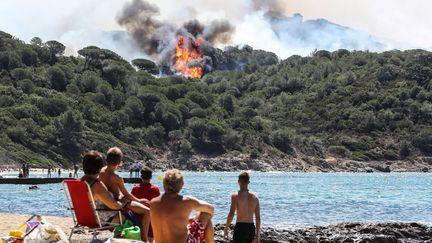 Des vacanciers profitent de la plage en regardant un feu de forêt à La Croix-Valmer, près de Saint-Tropez (Var), le 25 juillet 2017. Quelque 24 500 hectares de végétation sont partis en fumée en France lors de cette année. (VALERY HACHE / AFP)