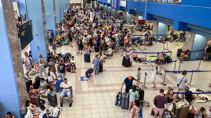 Des touristes attendent dans le hall des départs de l'aéroport sur l'île grecque de Rhodes alors que des évacuations sont en cours en raison d'incendies de forêt, le 23 juillet 2023. (WILL VASSILOPOULOS / AFP)