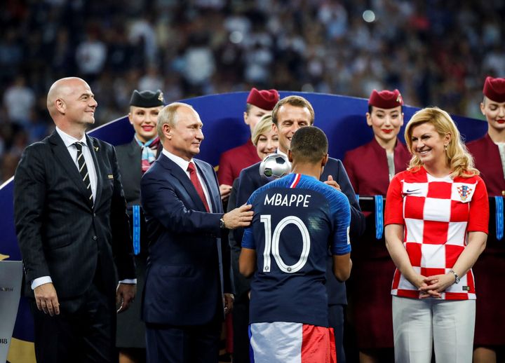 Emmanuel Macron (2e à d.), la présidente croate, Kolinda Grabar-Kitarovic (à d.), Vladimir Poutine (2e à g.) et le président de la FIFA Gianni Infantino (à ga.) saluent Kylian Mbappé, lors de la finale de la Coupe du monde&nbsp;remportée par la France, à Moscou, le 15 juillet 2018. (SEBNEM COSKUN / ANADOLU AGENCY / AFP)