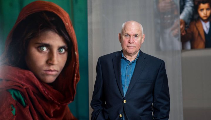 Le photographe américain Steve McCurry le 2 mars 2017 à Bruxelles (Belgique) à côté de la photo de la jeune Afghane qu'il a immortalisée et qui a fait le tour du monde. (DAMIEN CAUMIANT / BELGA MAG / AFP)