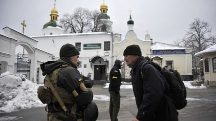 Un membre des forces de sécurité ukrainiennes discute avec un visiteur de la laure des Grottes de Kiev, le 22 novembre 2022. (SERGEI CHUZAVKOV / AFP)