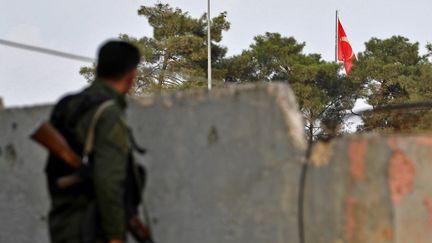 Un combattant kurde observe un drapeau turc de l'autre côté de la frontière, depuis la ville de Kobané, en octobre 2019 (AFP)