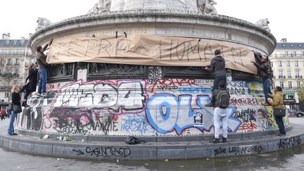 Des Parisiens déploient une banderole "J'être humain", sur la statue de la place de la République. (UWE ANSPACH / DPA / AFP)