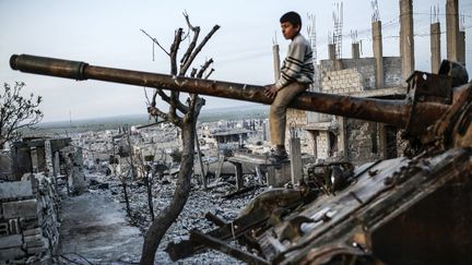 Un enfant syrien assis sur le canon d'un char d&eacute;truit, &agrave; Kobani (Syrie), le 26 janvier 2015.&nbsp; (YASIN AKGUL / AFP)