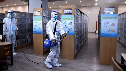 Un employé pulvérise du désinfectant dans une librairie de Qingdao, dans l'est de la Chine, le 13 mars 2022. (STR / AFP)