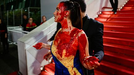 Une femme aux couleurs de l'Ukraine, couverte de faux sang, se fait évacuer du tapis rouge par un agent de sécurité (Cannes, le 21 mai 2023) (CHRISTOPHE SIMON / AFP)