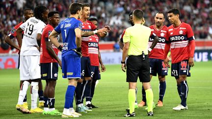 Les joueurs de Lille et de Nice qui entourent l'arbitre de la rencontre de Ligue 1, le 31 août 2022, alors qu'il discute avec l'arbitre responsable de la VAR. (FLAVIU BUBOI / AFP)