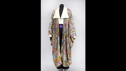 « DIAGHILEV ». Blouse en satin duchesse champagne, encolure en pointe agrémentée d’un large revers sur boutonnage bijou façon améthyste puis pression cachée, rappel sur les poignets droits et sur les poches poitrine à revers.
 (DR)