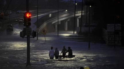 Des habitants de Houston (Texas) marchent les pieds dans l'eau lors des inondations provoquées par la tempête Harvey, le 28 août 2017. (NICK OXFORD / REUTERS)