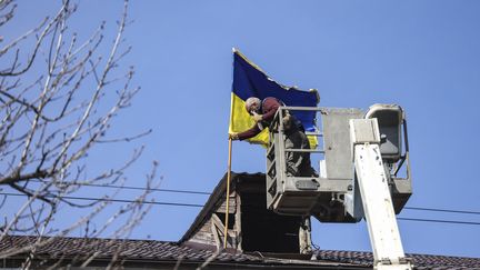 Un employé hisse le drapeau ukrainien sur l'hôtel de ville de Bucha, dans l'ouest de Kiev, le 7 avril 2022. (RONALDO SCHEMIDT / AFP)