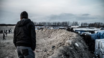 Un jeune migrant regarde ses amis jouer au volley-ball à l'entrée de la jungle de Calais (Pas-de-Calais), le 19 février 2016. (JULIEN PITINOME / NURPHOTO / AFP)