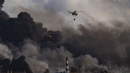 Un hélicoptère transportant des pompiers jette de l'eau sur les flammes, alors que l'incendie s'est propagé dans un deuxième réservoir, le 8 août 2022.&nbsp; (YAMIL LAGE / AFP)