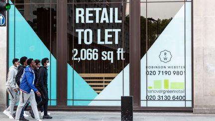 Un groupe de jeunes hommes&nbsp;passent devant la vitrine d'un magasin à louer sur Oxford Street, à Londres (Royaume-Uni), le 11 août 2020.&nbsp; (DOMINIKA ZARZYCKA / NURPHOTO / AFP)