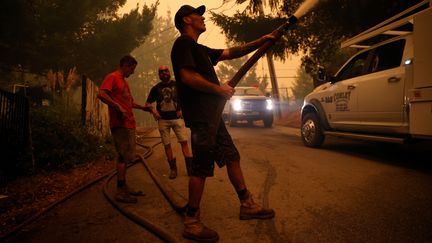 Des volontaires arrosent un bâtiment pour le protéger des flammes à l'extérieur de Santa Cruz (Californie), le 20 août 2020. (STEPHEN LAM / REUTERS)