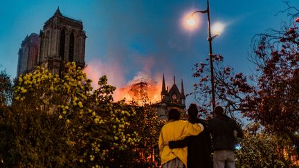 Des passants regardent, sidérés, les flammes qui embrasent la cathédrale Notre-Dame de Paris, le 15 avril 2019, depuis le square René-Viviani (5e arrondissement), à une centaine de mètres de là.&nbsp; (SIMON GUILLEMIN / HANS LUCAS)