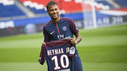 La star brésilienne Neymar pose avec le maillot du Paris Saint-Germain sur la pelouse du Parc des Princes, le 4 août 2017. Le club parisien a agité le mercato estival en rachetant la clause liant l'attaquant au FC Barcelone pour un montant record de 222 millions d'euros. (LIONEL BONAVENTURE / AFP)