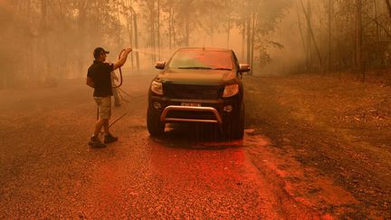 Un homme asperge sa voiture de retardateur de feu à Werombi, à 50 kilomètres au sud-ouest de Sydney, en Australie, le 6 décembre 2019. (STRINGER / REUTERS)