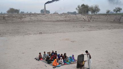 Un enseignant donne un cours en plein air &agrave; des &eacute;l&egrave;ves dans un camp de r&eacute;fugi&eacute;s pr&egrave;s de Jalalabad (Pakistan), le 1er d&eacute;cembre 2013. (NOORULLAH SHIRZADA / AFP)