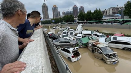 Des personnes regardent des voitures englouties par les eaux après les fortes pluies qui ont frappé la ville de Zhengzhou, dans la province centrale du Henan, en Chine, le 21 juillet 2021. (STR / AFP)