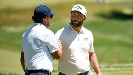 Phil Mickelson (à gauche) sert la main de Jon Rahm, lors d'un entraînement à l'US Open, le 15 juin 2022. (JARED C. TILTON / AFP)