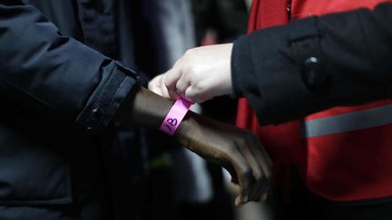 Un employé de l'Office français de l'Immigration et de l'intégration (Ofii) attache un bracelet rose autour du poignet d'un migrant, lundi 24 octobre 2016. La couleur des bracelets correspond à une région française. (EMILIO MORENATTI / AP / SIPA)