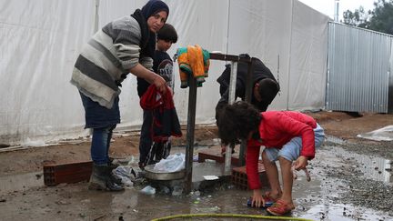 Les pieds dans la boue, une mère et ses deux enfants lavent des vêtements dans le camp d'Idomeni. (MAXPPP)