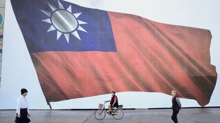 Des passants devant le drapeau taïwannais, le 13 janvier 2024, jour de vote sur l'île. (SAM YEH / AFP)