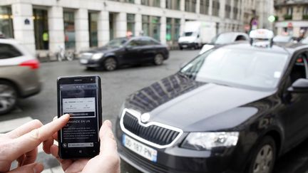 Un client consulte l'application Uber&nbsp;sur son smartphone devant un taxi &agrave; Paris le 10 d&eacute;cembre 2014. (ELIOT BLONDET / AFP)