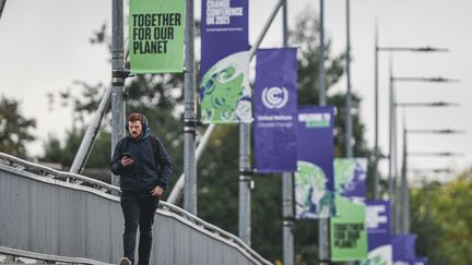 Un homme passe sur un pont sur lequel sont installés des drapeaux de la COP26, à Glasgow (Ecosse), le 1er septembre 2021.&nbsp; (EWAN BOOTMAN / NURPHOTO / AFP)