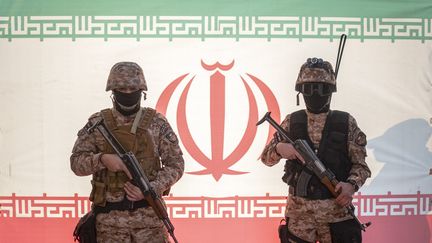 Deux gardiens de la révolution islamique posent devant un drapeau iranien, le 29 décembre 2022, à Téhéran. (MORTEZA NIKOUBAZL / NURPHOTO / AFP)