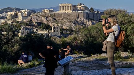 Des touristes profitent de la vue sur l'Acropole à Athènes, le 12 avril 2022. (LOUISA GOULIAMAKI / AFP)