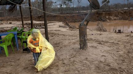 Johan, 5 ans, s'abrite de la pluie avec le poncho de son p&egrave;re dans le campement pour mineurs &agrave; La Pampa (P&eacute;rou), le 5 mai 2014. (RODRIGO ABD / AP / SIPA)