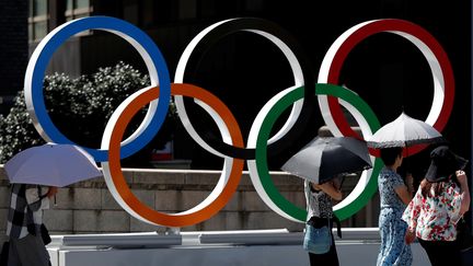 Des passants devant les anneaux olympiques, dans le quartier de&nbsp;Nihonbashi à Tokyo (Japon), le 5 août 2019. (ISSEI KATO / REUTERS)