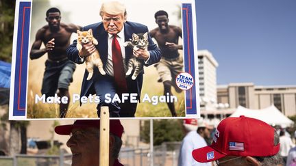 Un homme brandit un visuel généré par IA illustrant une fausse information raciste propagée par Donald Trump, lors d'un rassemblement électoral pour le candidat républicain à Tucson (Arizona), le 12 septembre 2024. (REBECCA NOBLE / AFP)