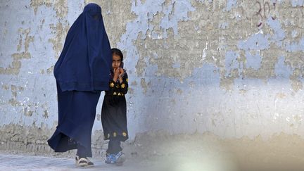 Une femme vêtue d'une burqa marche avec une fillette dans une rue de Kaboul (Afghanistan), le 7 mai 2022. (AHMAD SAHEL ARMAN / AFP)