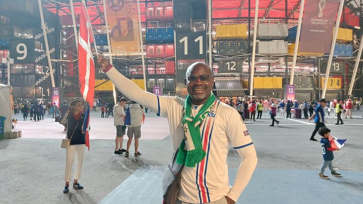 Osita, supporter nigérian, portant l'écharpe de son pays, un maillot de l'Islande et brandissant un drapeau du Danemark, avant France-Danemark, le 26 novembre à Doha (Qatar). (PIERRE GODON / FRANCEINFO)