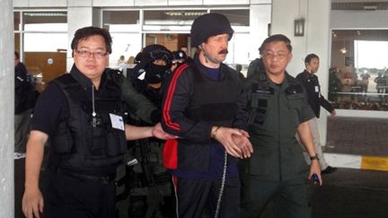 Deux hommes escortent Viktor Bout à l'aéroport de Bangkok, durant son extradition (16/11/2010) (AFP / local press)