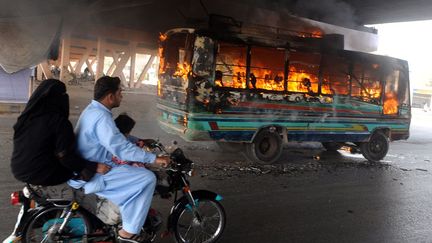 Un couple &agrave; moto passe &agrave; c&ocirc;t&eacute; d'un bus incendi&eacute; par des manifestants &agrave; Karachi (Pakistan), le 27 mars 2012. (RIZWAN TABASSUM / AFP)