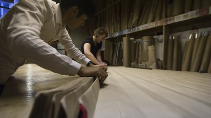 Léopoldine Pataa étale un métier sur une grande table pour faire un plissé soleil. Elle glisse avec minutie le tissu entre les deux feuilles de carton, comme un très grand éventail ouvert, puis les replie. Le métier sera ensuite placé dans une étuve, entre 85 et 100°, pendant une durée allant de 2 à 5 heures selon les tissus. Il faudra encore laisser reposer plusieurs heures. "Pour une pièce, il faut une bonne journée", explique Nadine Duffat, directrice de Lemarié. Certaines peuvent aussi être plissées à la machine.
 (JOEL SAGET / AFP)