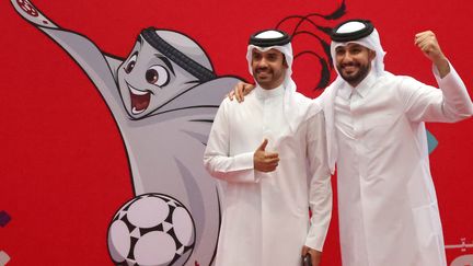 Deux Qatariens posent à côté d'une illustration de la mascotte de la Coupe du monde de la Fifa, à Doha,&nbsp;le 16 octobre 2022. (KARIM JAAFAR / AFP)