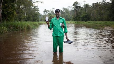 Leon Koli, garde forestier du WWF, debout dans l'eau alors qu'il pose pour une photo avec son smartphone, dans le parc national de Dzanga-Ndoki, à Bayanga, au sud-ouest de la République centrafricaine, le 1er novembre 2018. Il utilise son smartphone pour rester en contact avec sa famille dans la capitale, mais aussi pour photographier des éléphants ou des gorilles traversant son chemin dans la jungle équatoriale profonde. (FLORENT VERGNES / AFP)