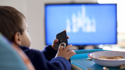 Un enfant mange devant la télévision. Photo d'illustration. (THANASIS ZOVOILIS / MOMENT OPEN / GETTY IMAGES)