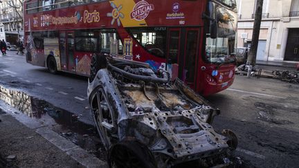 Un bus touristique passe le 2 décembre 2018 devant une voiture brûlée après le rassemblement des "gilets jaunes" la veille à Paris. (MAXPPP)