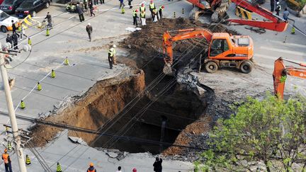 Des hommes tentent de remplir un trou apparu dans la chauss&eacute;e de la rue&nbsp;Shiliuzhuang, &agrave; P&eacute;kin (Chine), le 26 avril 2011. La cavit&eacute; s'est cr&eacute;&eacute;e &agrave; cause de la construction d'une ligne de m&eacute;tro. ( AFP )